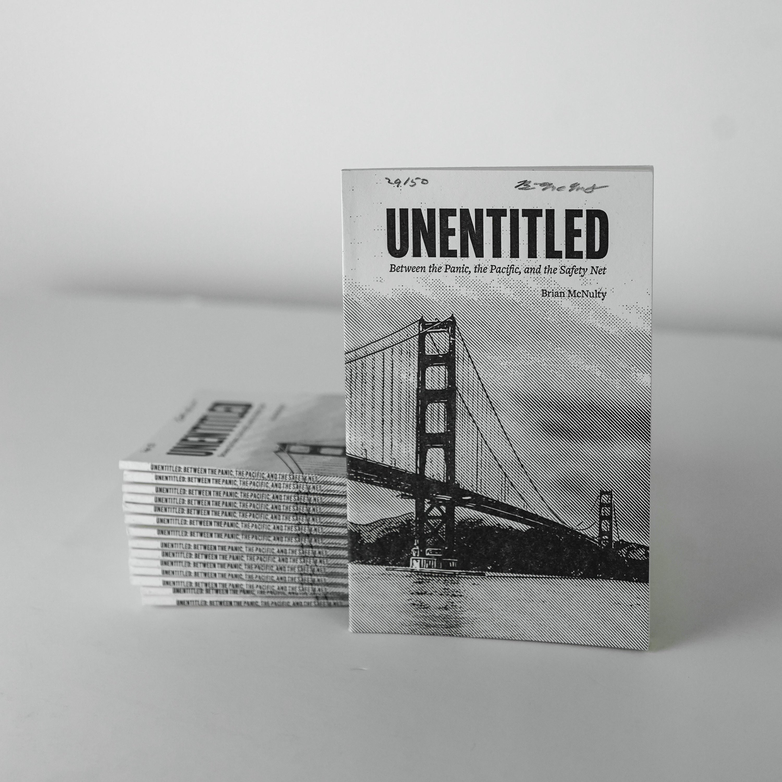 Stack of books titled 'UNENTITLED' with a black and white image of a bridge on the cover.
